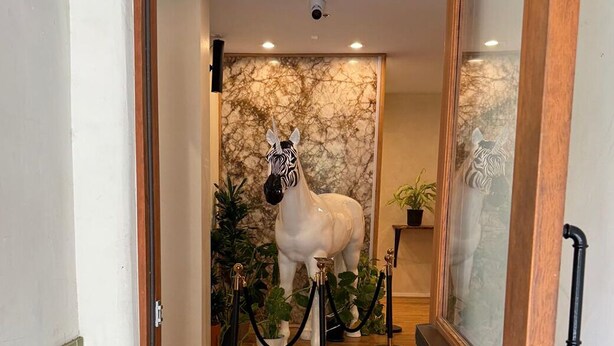 Une statue de cheval blanc se trouve dans un couloir, avec un mur en marbre et des plantes en pot.