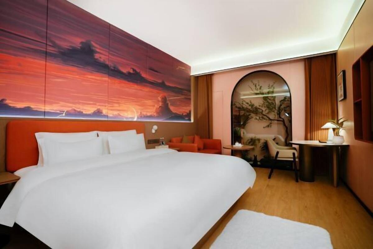 Une chambre d’hôtel dotée d’un grand lit, d’un coin salon avec un canapé et des fauteuils, d’un bureau et d’un grand tableau accroché au mur.