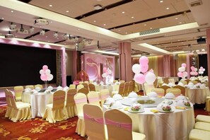 Une salle de banquet avec des tables rondes, des chaises et une scène décorée de ballons.