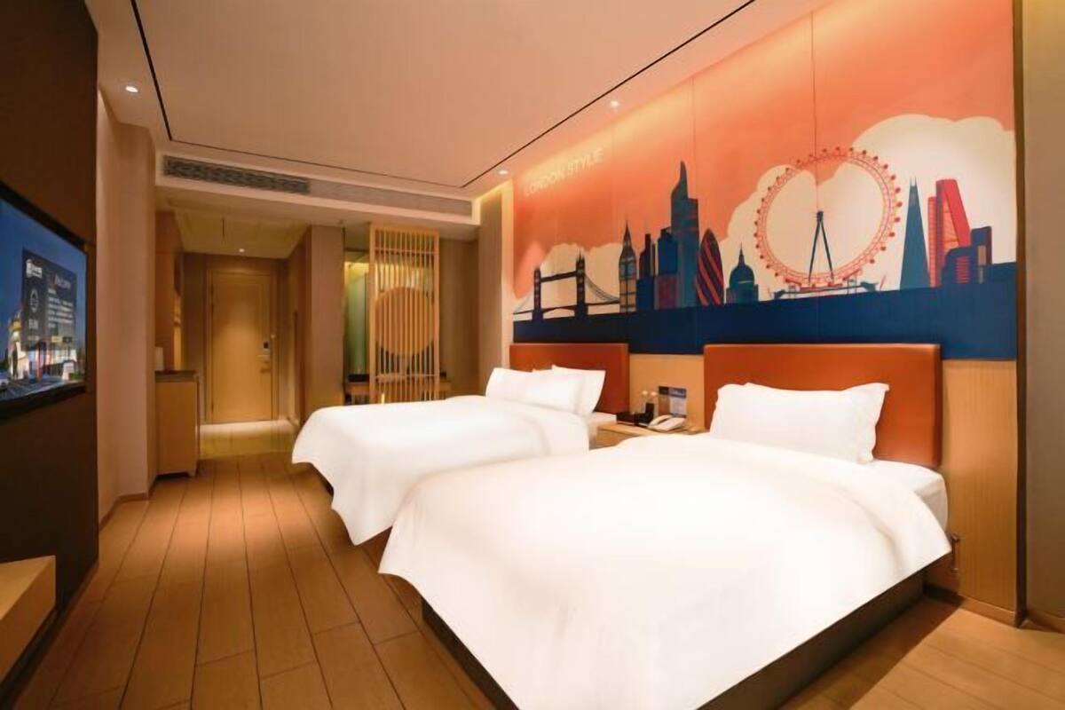 Une chambre d’hôtel avec deux lits, une fresque représentant un paysage urbain, un téléviseur et un plancher en bois.