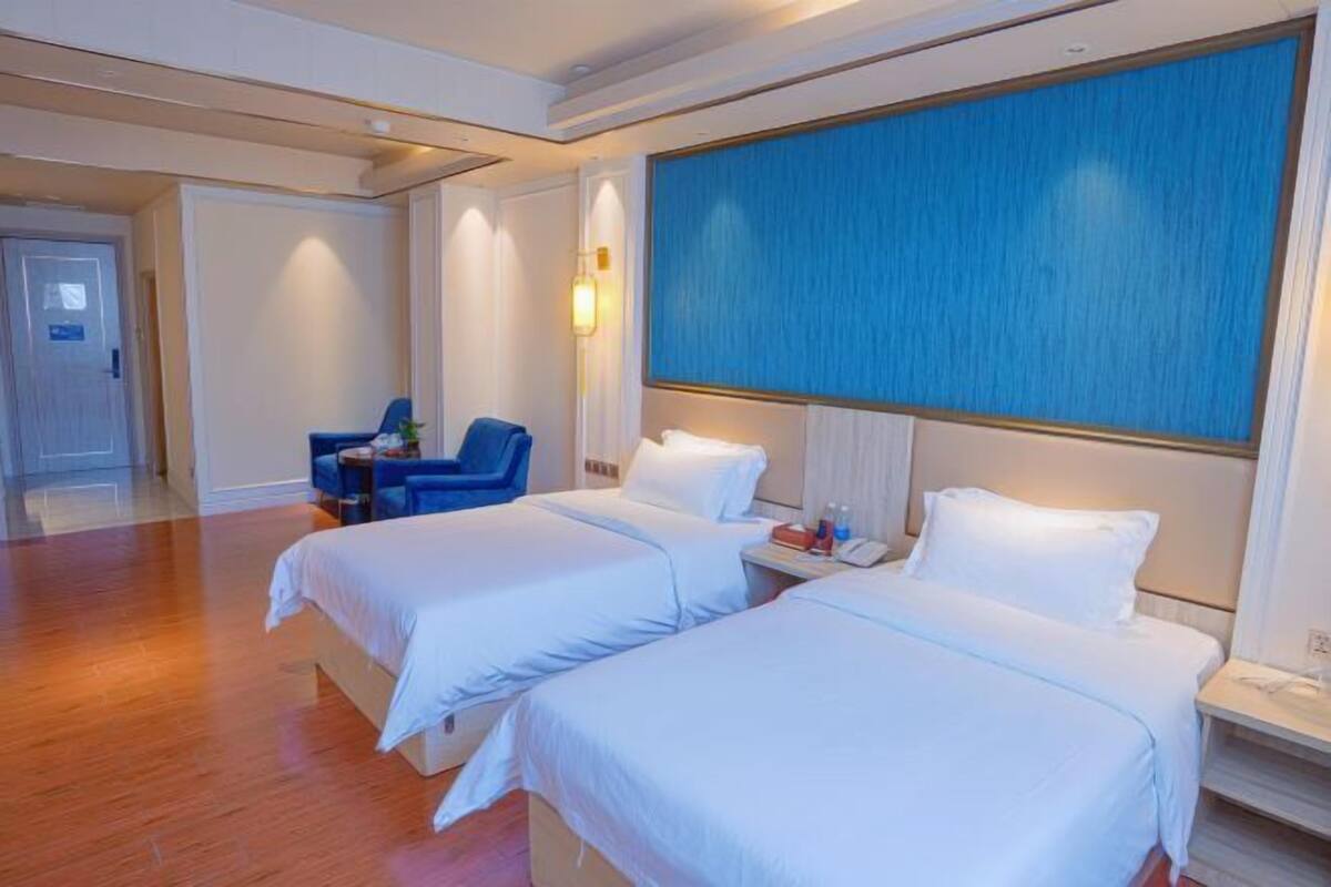Une chambre d’hôtel avec deux lits, un bureau, une chaise et une grande fenêtre.