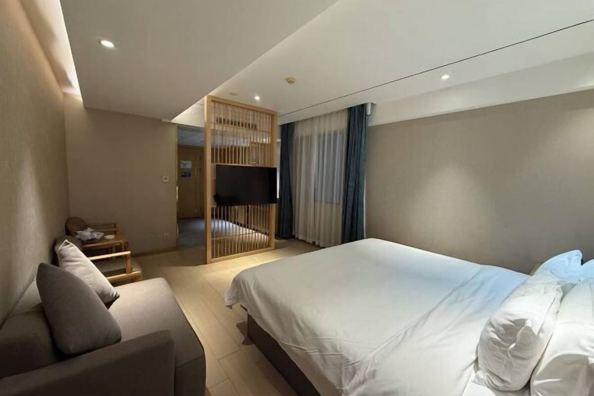 Une chambre d’hôtel avec un lit, un canapé, une télévision et une cloison en bois.