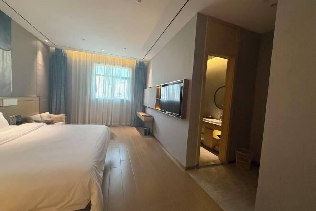 Une chambre d’hôtel avec un grand lit, un téléviseur fixé au mur, un petit bureau et une salle de bain visible à travers une porte ouverte.