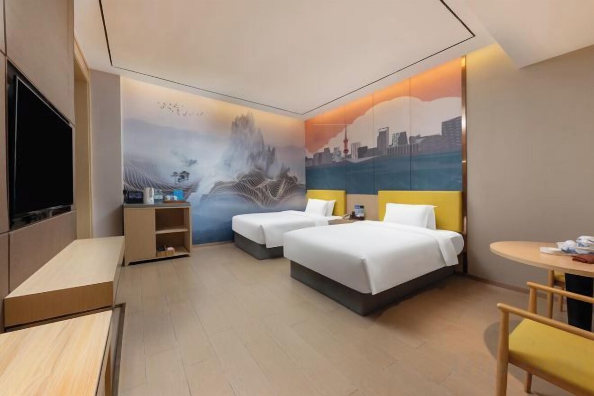A hotel room with two beds, a desk, a chair, and a TV.