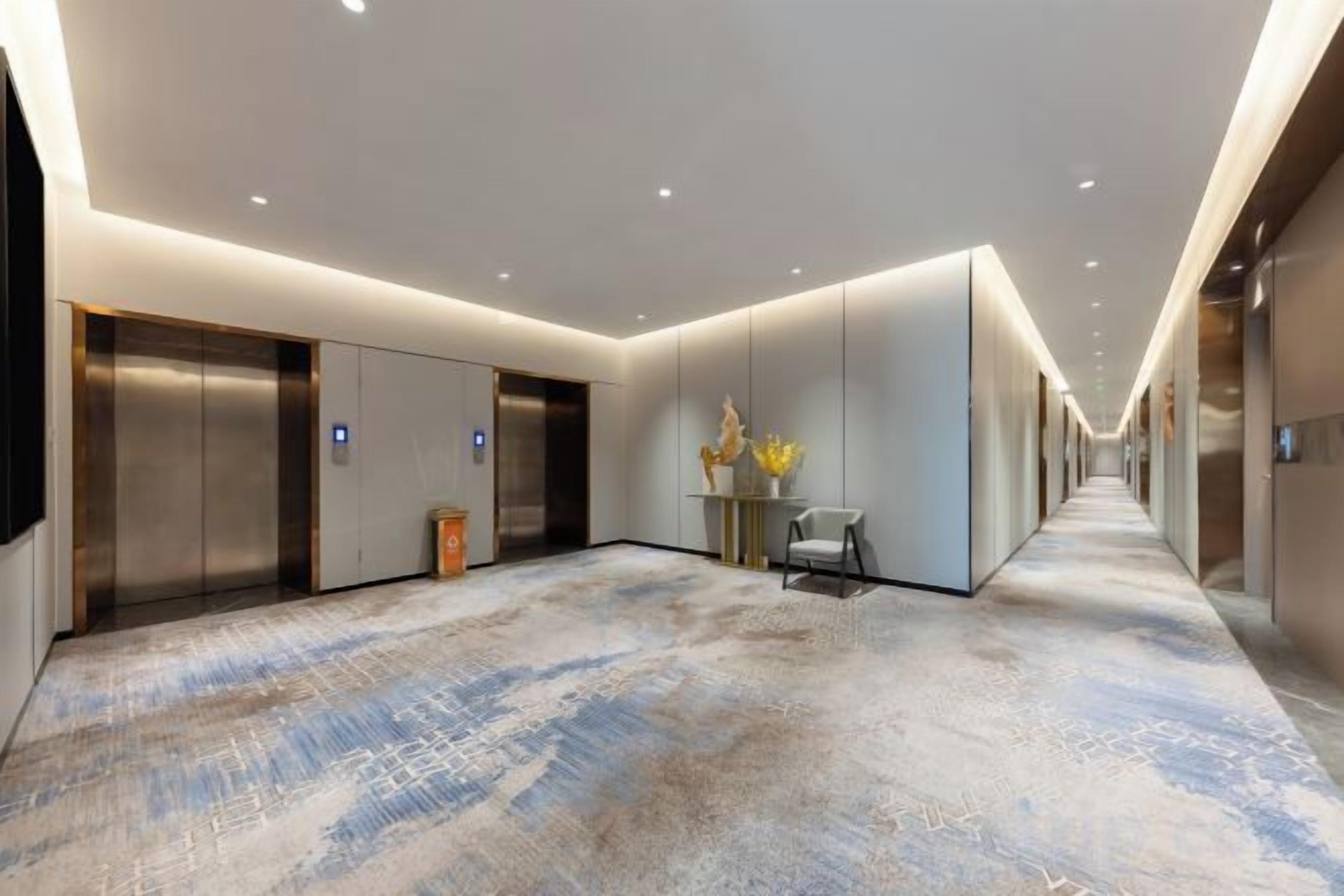 Un pasillo de hotel con ascensores, una recepción y una alfombra estampada.