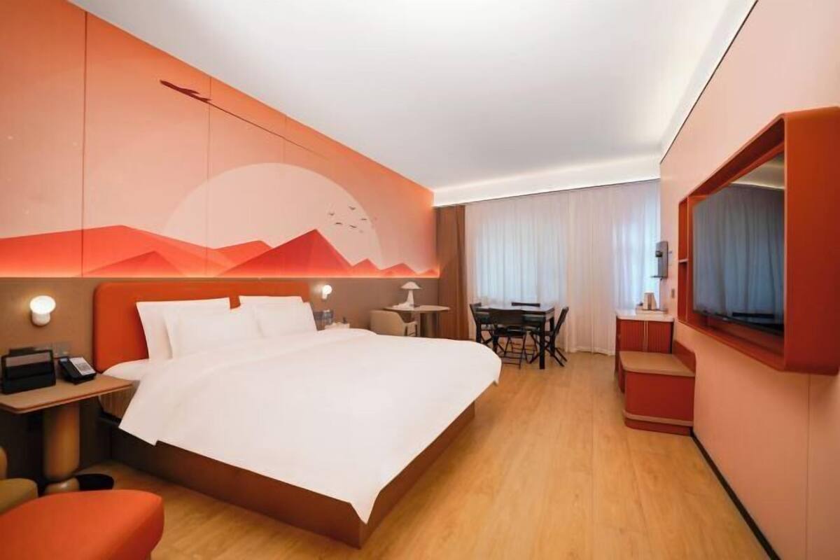 Une chambre d’hôtel équipée d’un lit, d’un bureau, d’une chaise, d’une télévision et d’un mur décoré avec un motif de montagne.