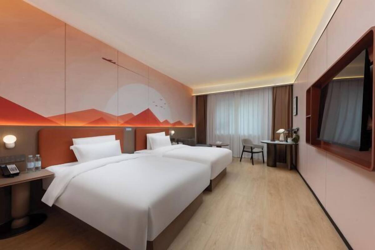 Une chambre d’hôtel avec deux lits, un bureau, une chaise et une grande fenêtre.