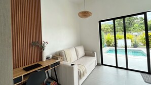 Un salon moderne avec un mur lambrissé en bois, un canapé beige, un bureau avec une chaise et une vue sur une piscine.