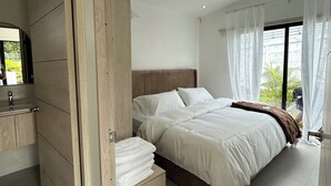 Une chambre moderne avec une armoire en bois, un lit avec une literie blanche et une salle de bain équipée d’un lavabo et d’un miroir.