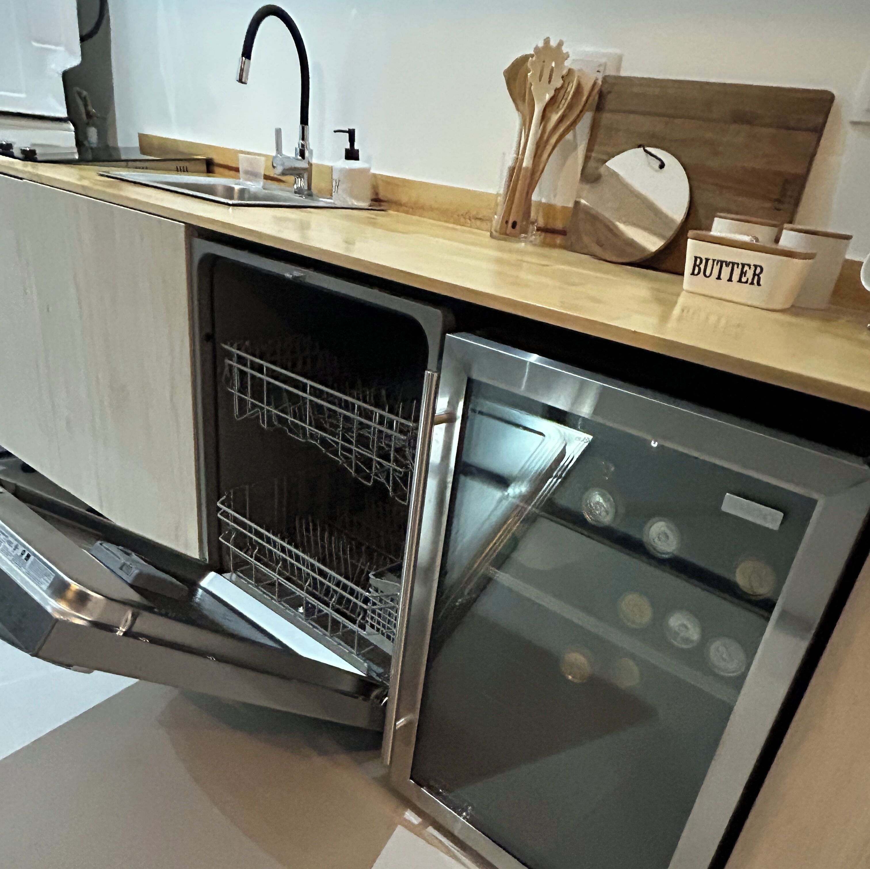 Une cuisine de taille réduite équipée d’un lave-vaisselle, d’un évier et d’un plan de travail en bois.