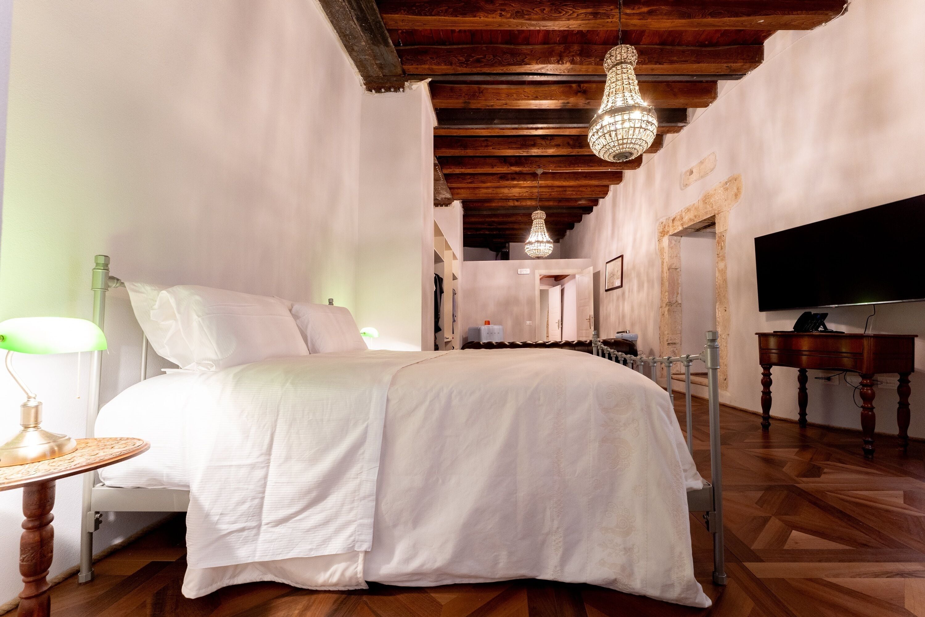 Ein Schlafzimmer mit einem Bett, Holzboden, einer Chandelüster, einem Fernseher und einem Holztisch.