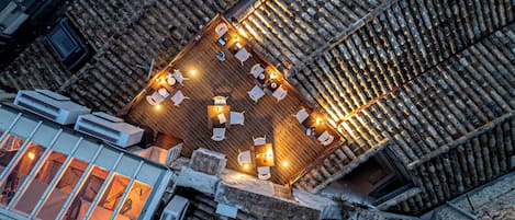 Una terraza en la azotea con piso de madera, varias mesas y sillas, y vistas de los edificios circundantes.