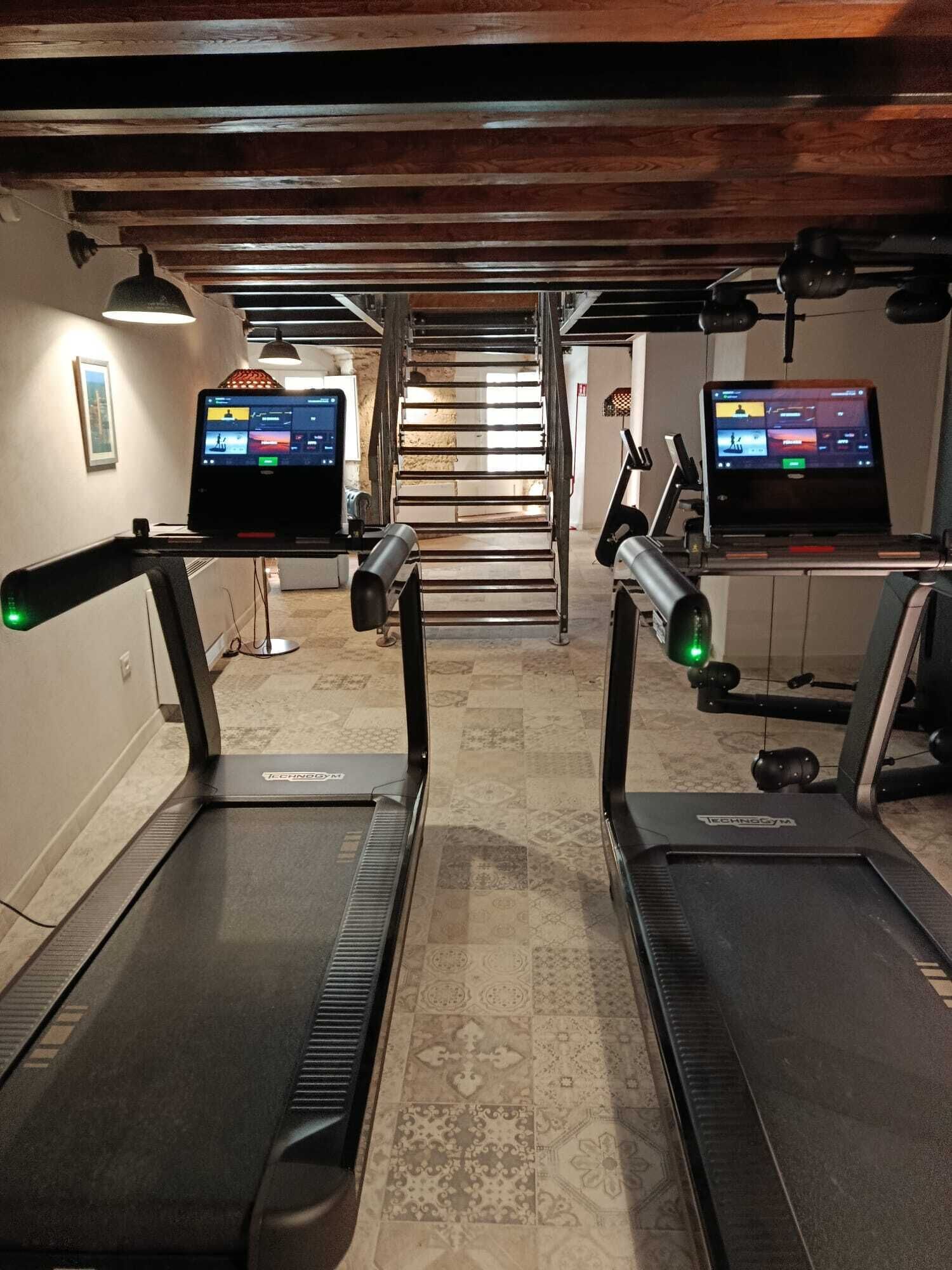 A gym with treadmills, a staircase, and two laptops on desks.