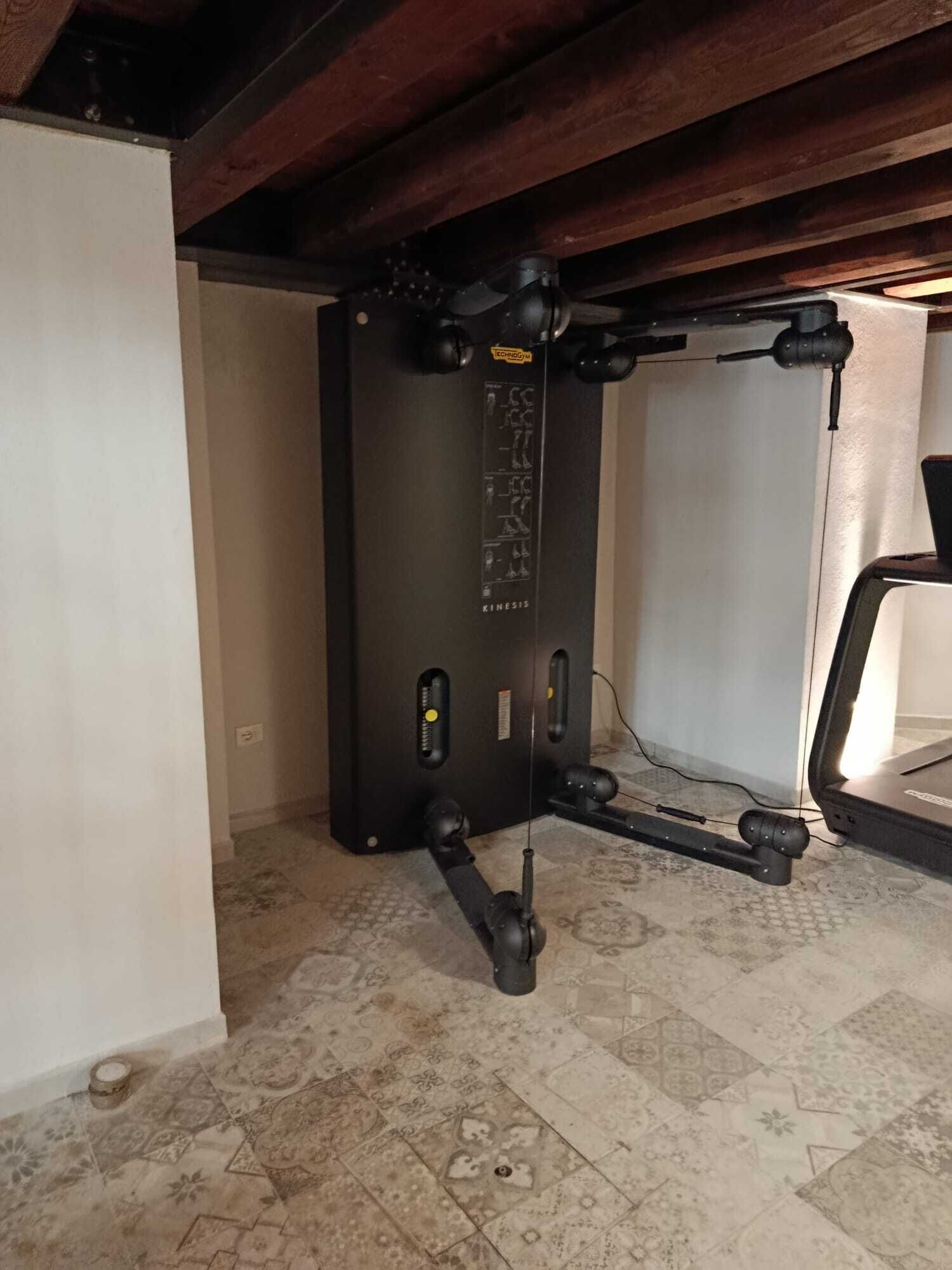 Een sportschool met een zwart krachttrainingsapparaat, een vloer met een patroon en een houten plafond.