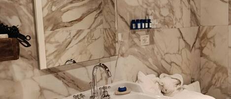 Un bagno con una parete in marmo, un lavandino su piedistallo in legno e uno specchio sopra il lavandino.