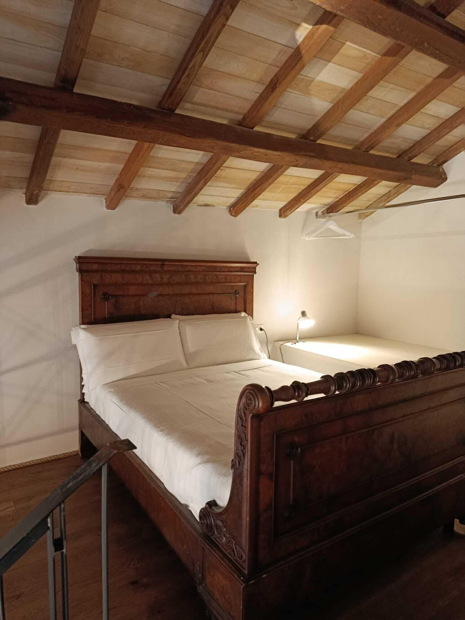 Ein Schlafzimmer mit einem hölzernen Bett, weißen Bettwäsche und einer schrägen Decke mit sichtbaren Balken.