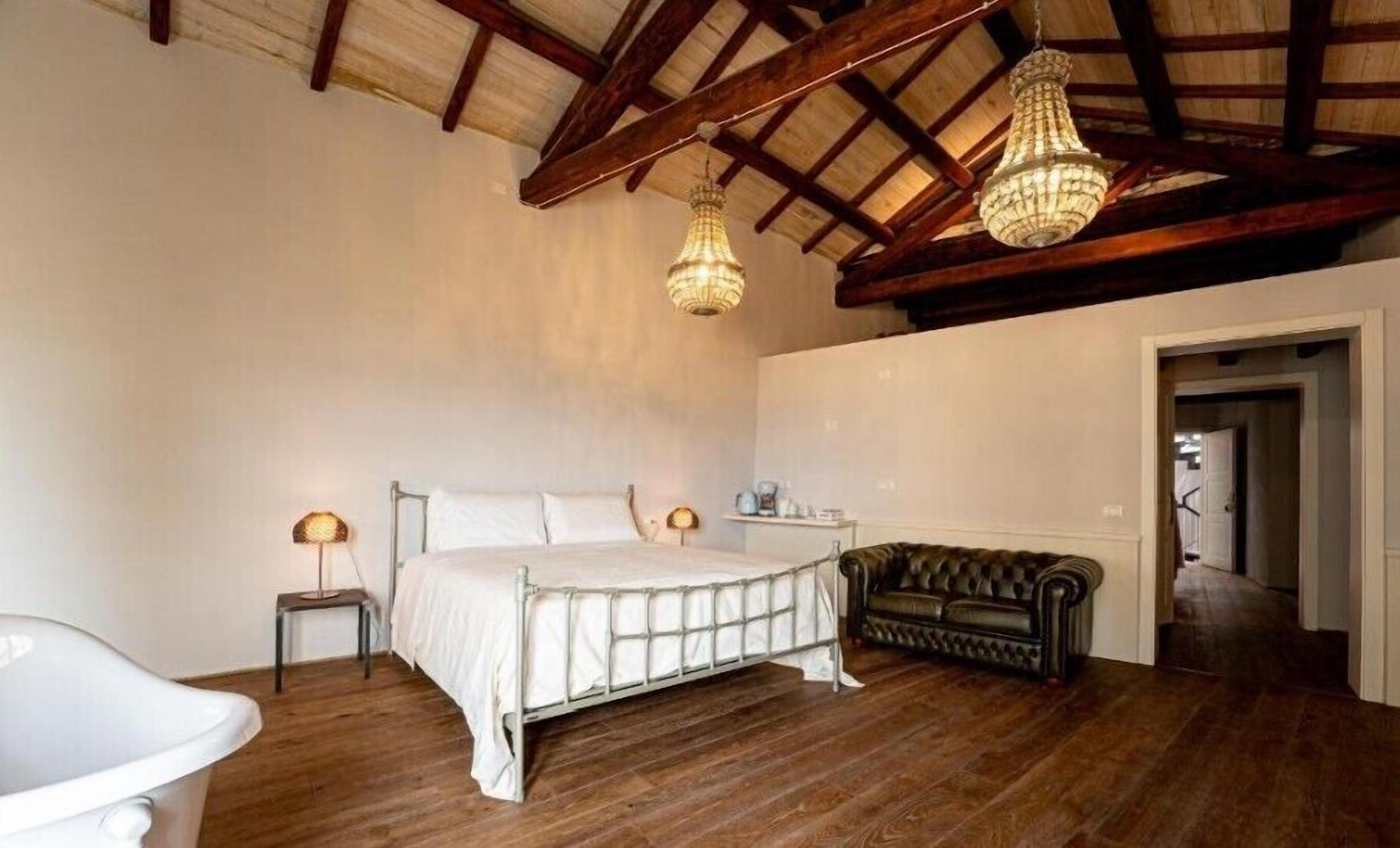A bedroom with a bed, bedside tables, a sofa, and a chandelier.