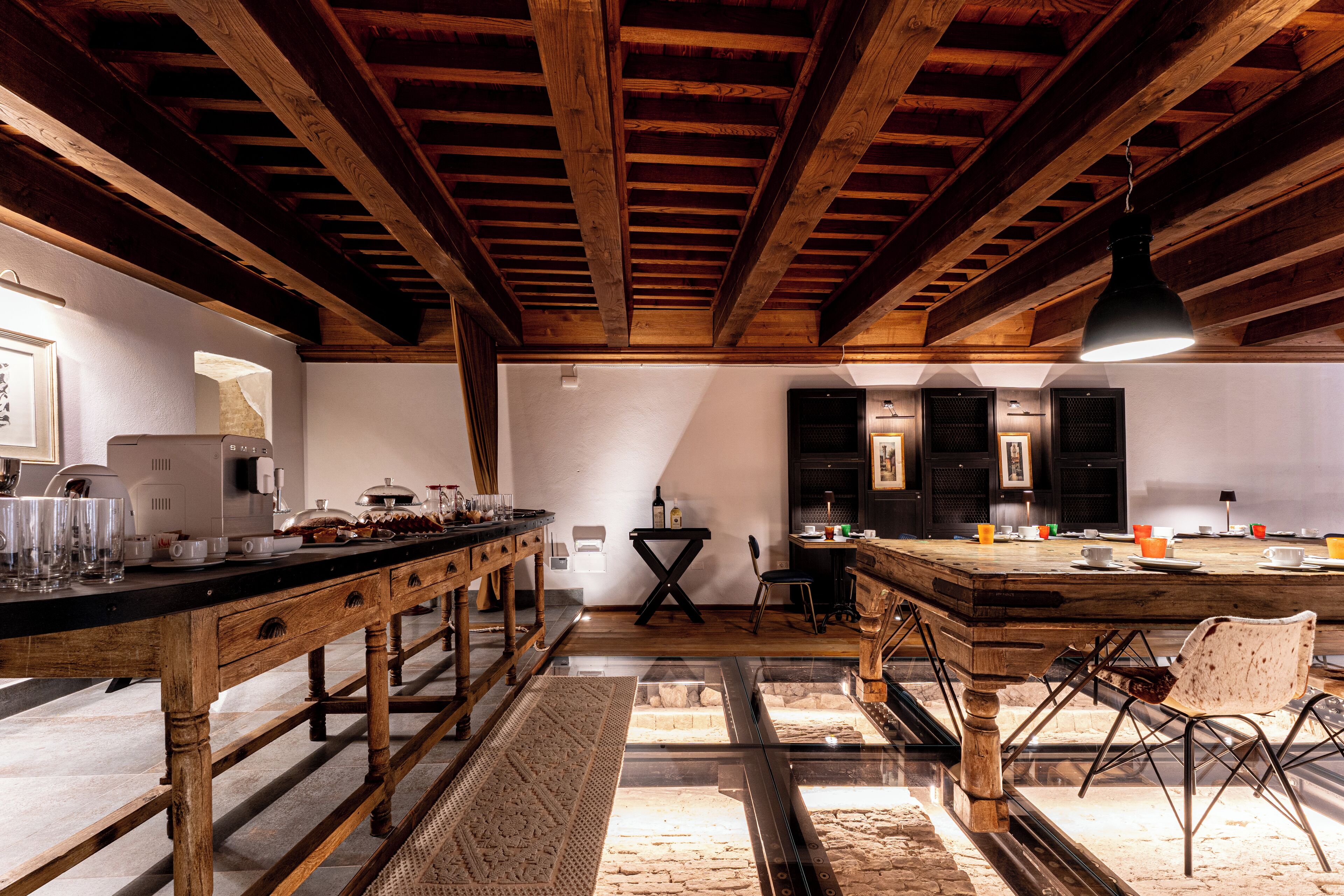A rustic kitchen with wooden beams, a long counter, and a dining area with chairs.