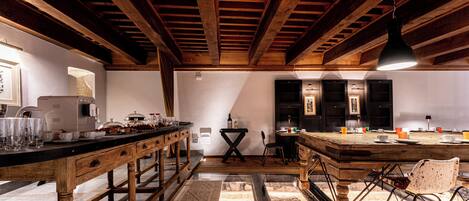 A rustic kitchen with wooden beams, a long counter, and a dining area with chairs.