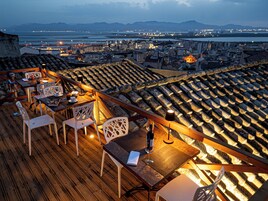 A rooftop terrace with wooden flooring, white chairs, and tables set up for dining.