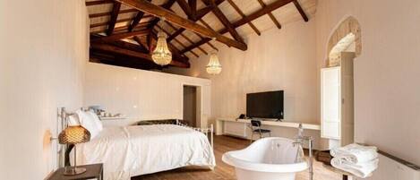 Une chambre avec un grand lit, une baignoire blanche et un téléviseur dans un coin.