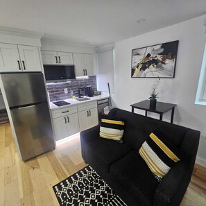 A compact living space with a kitchenette, a black sofa with patterned cushions, a small side table, and a painting on the wall. - The Mini-Lux B. at Lower Atwells Avenue Laundry & Dishwasher Close to DT (Providence)
