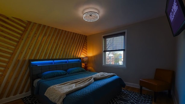 A bedroom with a bed, a chair, a window with blinds, and a ceiling light fixture. - Treehouse Suite | King BR | Spa bath | Calm Energy (Parkville)