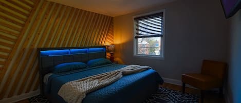 Une chambre à coucher comprenant un lit, une chaise, une fenêtre avec des stores et un luminaire au plafond.