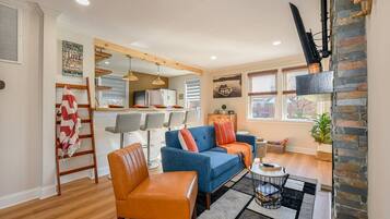 A modern living room with a blue sofa, a wooden chair, and a kitchen area in the background.