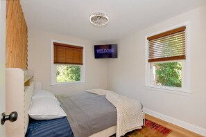 A bedroom with a bed, a TV mounted on the wall, and two windows with blinds. - Treehouse Suite | King BR | Spa bath | Calm Energy (Parkville)