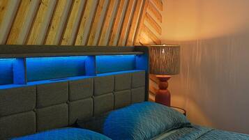 A bedroom with a sloped ceiling, a bed with a headboard, and a bedside lamp.