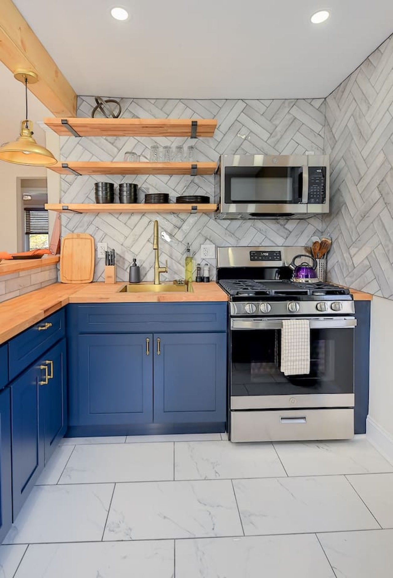 A modern kitchen with blue cabinets, a stainless steel stove, and a microwave.