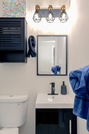 Un baño moderno con un lavabo blanco, un mueble negro, un espejo y tres lámparas colgantes geométricas.