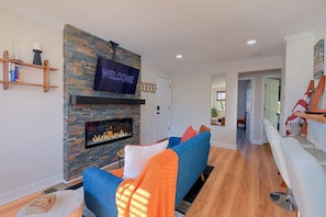A modern living room with a stone fireplace, a flat-screen TV, and a blue sofa with orange throw pillows. - Treehouse Suite | King BR | Spa bath | Calm Energy (Parkville)