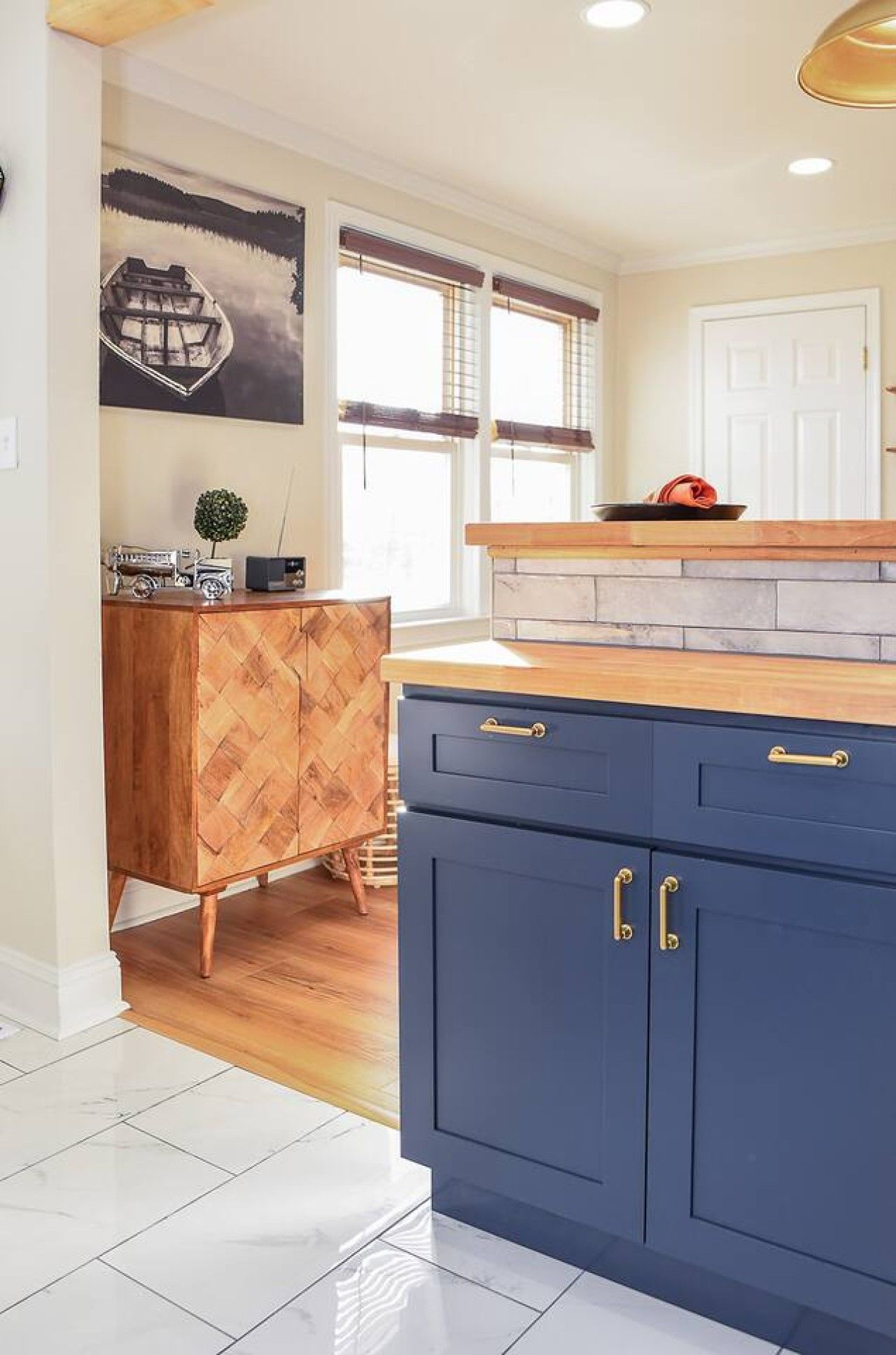 A kitchen with a wooden herringbone cabinet, a blue cabinet with gold handles, and a painting of a boat on the wall.