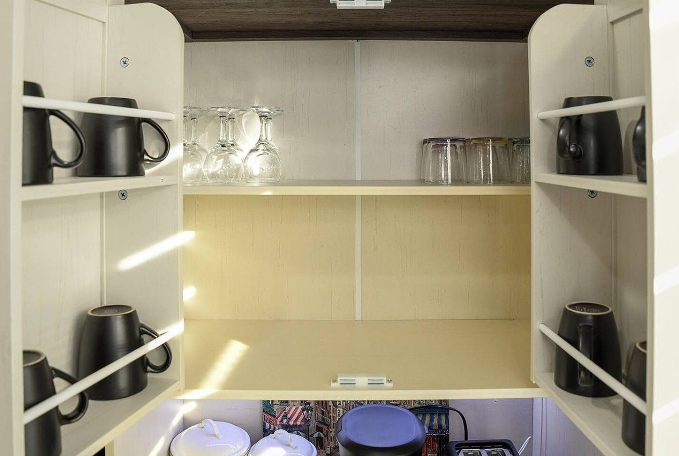 A kitchen with shelves holding mugs, glasses, and a kettle.