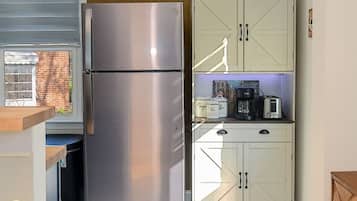A compact kitchen with a stainless steel refrigerator, a wooden cabinet with kitchen appliances, and a window with a view of a brick building.