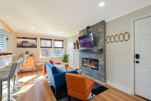 A living room with a fireplace, a television mounted above it, and a sofa. - Treehouse Suite | King BR | Spa bath | Calm Energy (Parkville)