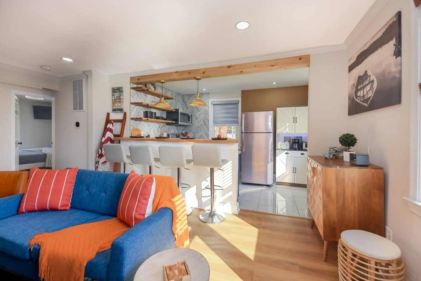 A modern living room with a sofa, a coffee table, and a kitchen area with a refrigerator, microwave, and wooden cabinets.