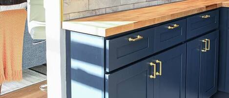 Cocina con armarios azul oscuro, encimera de madera e iluminación colgante.