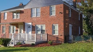 A two-story brick house with a front porch and a small front yard. - Treehouse Suite | King BR | Spa bath | Calm Energy (Parkville)