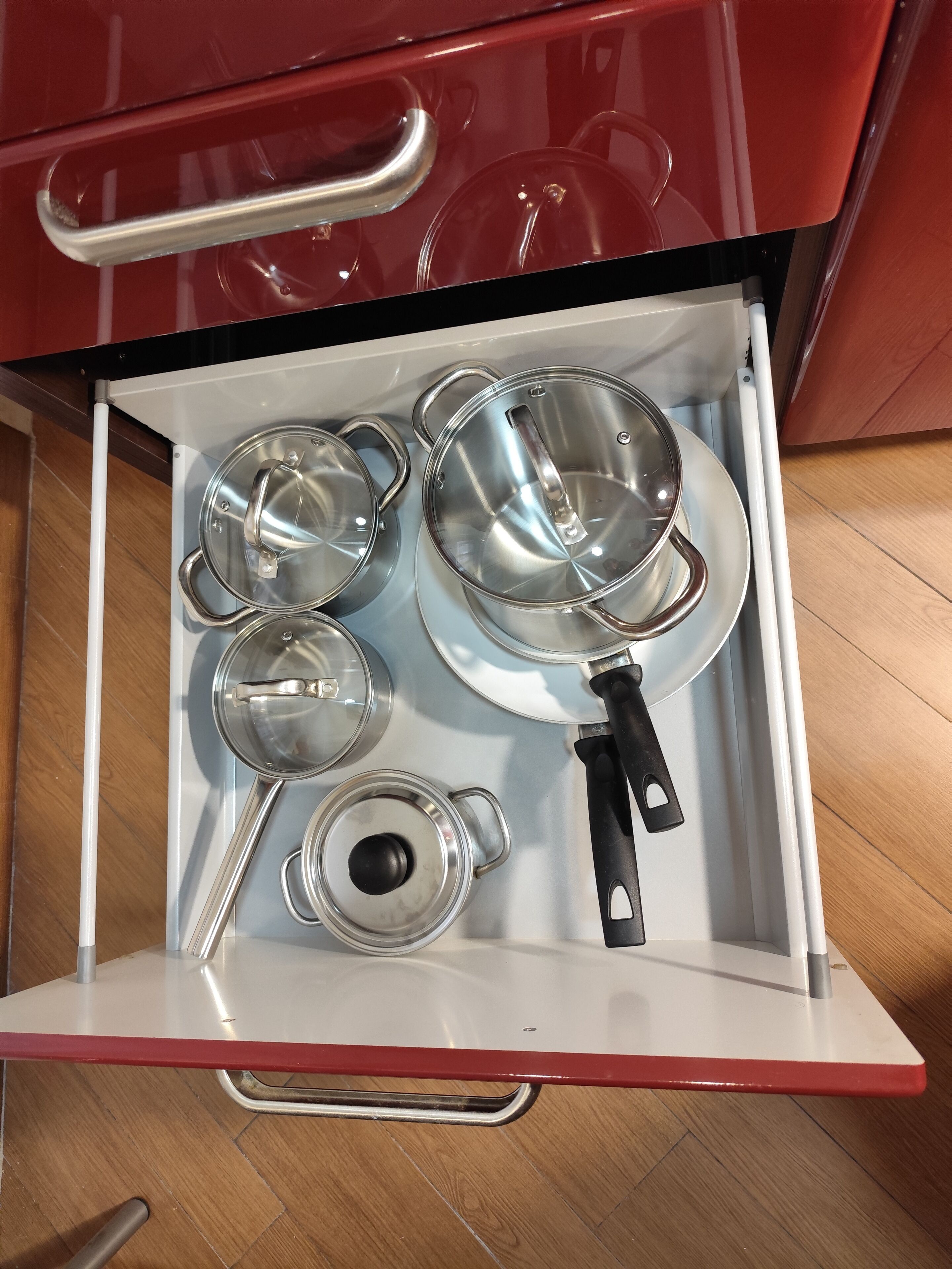 A kitchen drawer with various stainless steel cookware including pots, pans, and a ladle.