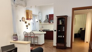 A living room with a dining area, a kitchen in the background, and a bookshelf.