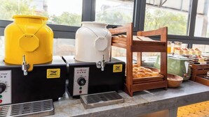 Un espace dédié au café, équipé de deux machines à café, d’un récipient jaune et d’une étagère en bois où sont disposées des pâtisseries.