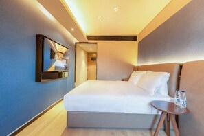 A hotel room with a bed, bedside table, and a mirror.
