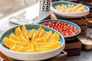 Una mesa de buffet con recipientes de naranjas en rodajas y frijoles rojos.