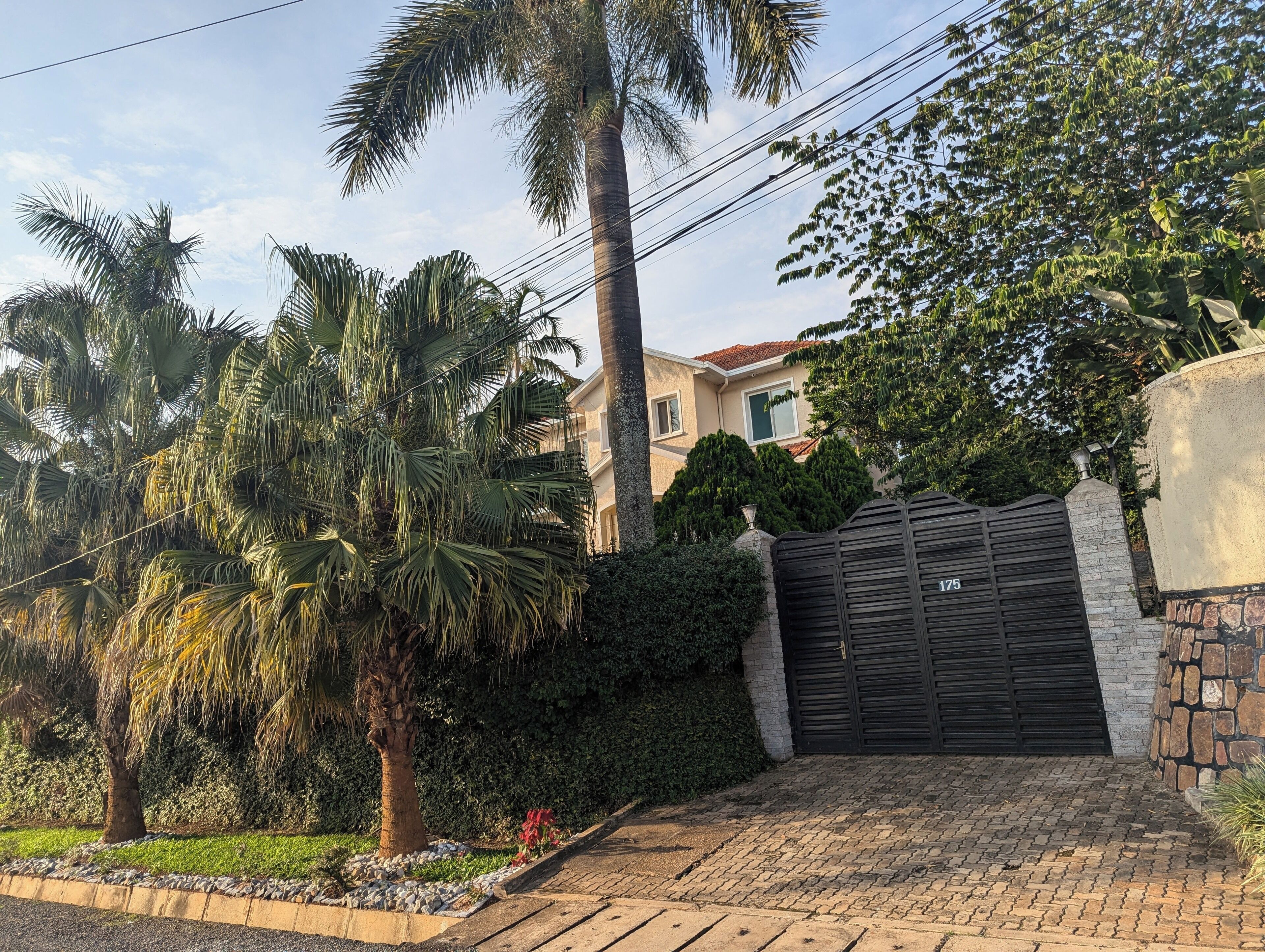 A residential property with a gated entrance, palm trees, and a well-maintained garden.