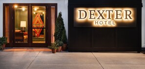 Ein Hotel Eingang mit einem Schild mit der Aufschrift 'DEXTER HOTEL', einer Glastür, einem kleinen Baum und einer Lampe im Inneren.