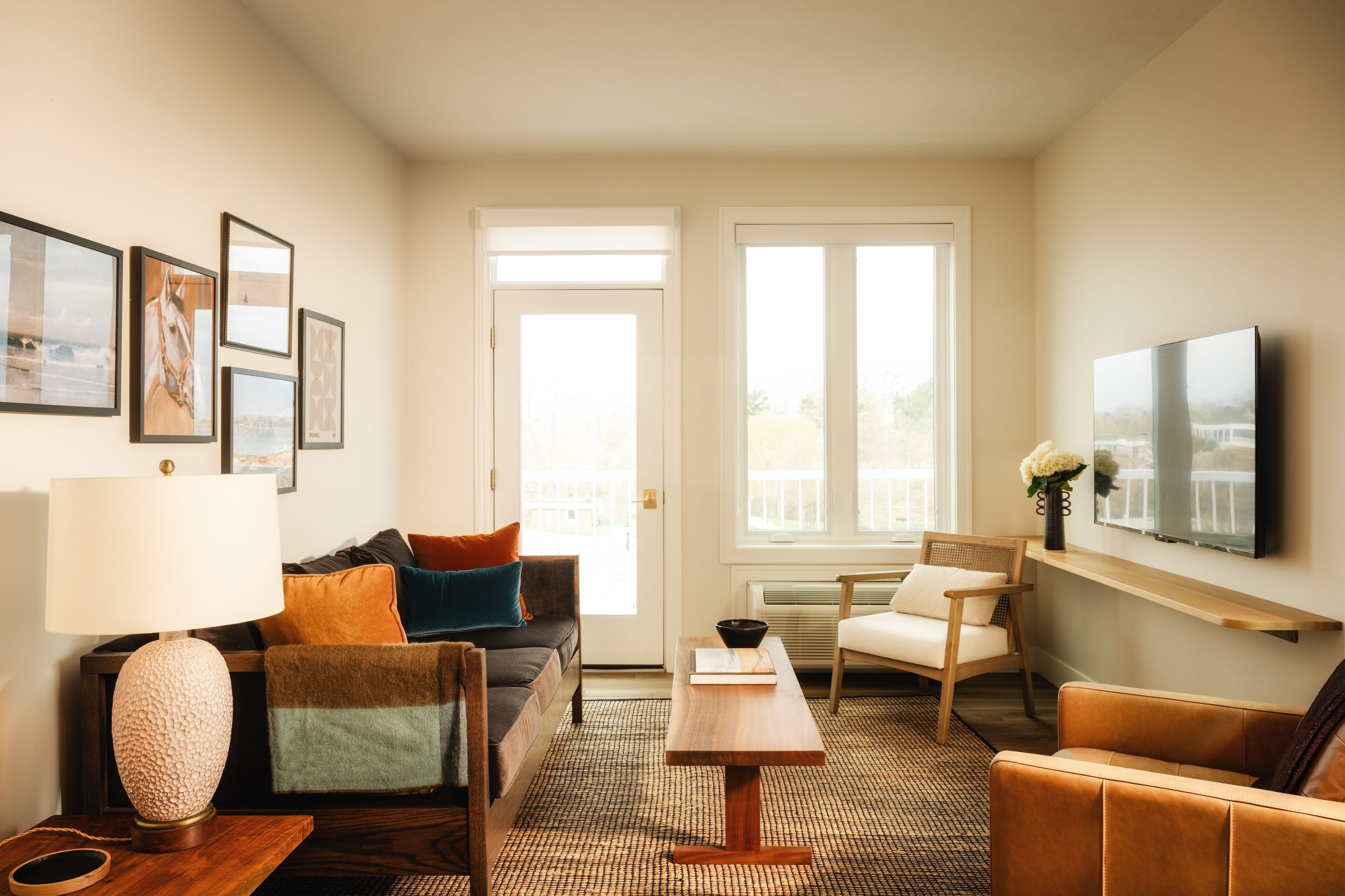 A living room with a sofa, armchair, coffee table, and a flat-screen TV mounted on the wall.