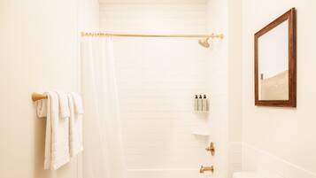 A bathroom with a bathtub, a toilet, a shower curtain, and a mirror.